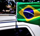 Bandeira do Brasil pequena verde e amarela fixada no teto de um carro branco.