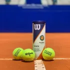 Bolas de tênis Wilson Roland Garros amarelas e lata em quadra de saibro.