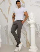 Homem veste calça masculina sarja cinza escura e camiseta branca, encostado em parede de mármore.