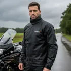 Homem com capa chuva motoqueiro preta e moto em estrada molhada.