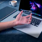 Mão segurando case para HD Slim transparente sobre laptop prateado.