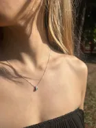 Mulher com colar Nossa Senhora Aparecida de prata no pescoço, cabelo loiro e blusa preta.