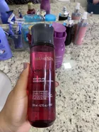 Mão segurando frasco vermelho-rosado de Colônia Nativa Spa Ameixa com tampa escura.