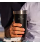 Mão segurando copo térmico Stanley preto fosco com borda prateada.