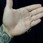 Corrente de prata com pingente crucifixo prateado em mão tatuada.