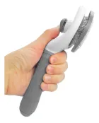 Mão segurando rasqueadeira automática cinza e branca com cerdas metálicas.