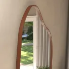 Espelho orgânico com moldura caramelo refletindo jardim em parede clara.