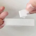 Mão removendo fita clareadora branca texturizada de um suporte claro.