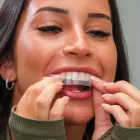 Mulher aplicando fitas clareadoras transparentes nos dentes.