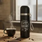 Garrafa térmica preta com 'coffee break' e xícara de café fumegante em mesa.
