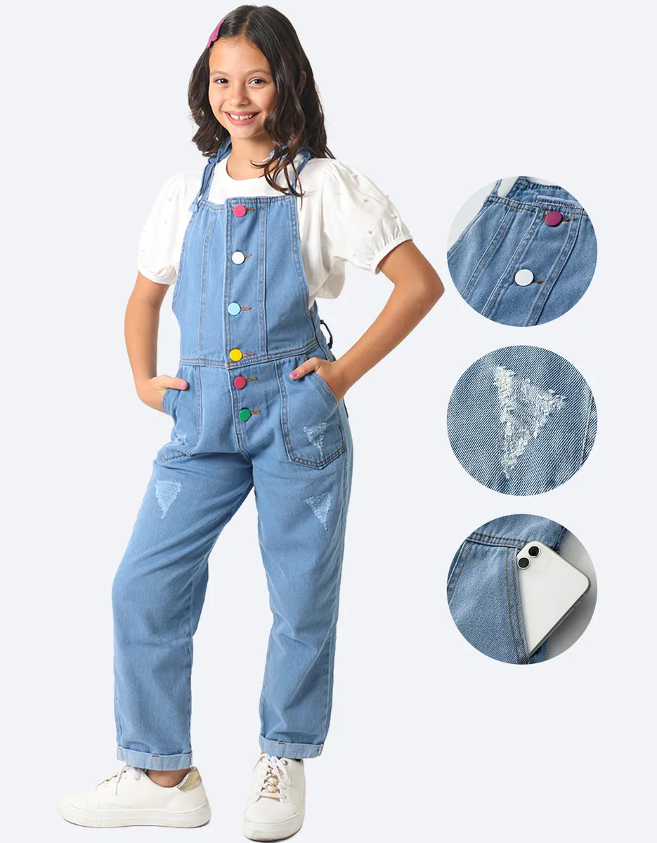 Menina vestindo jardineira macacão jeans azul claro, com botões coloridos e rasgos.