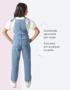 Jardineira jeans azul clara em menina de costas com blusa branca