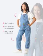 Menina veste jardineira jeans azul clara com botões coloridos e rasgos.