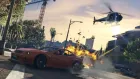 Grand Theft Auto V: Carro laranja explodindo na rua com helicóptero preto voando