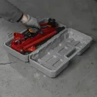 Macaco hidráulico tipo jacaré vermelho em caixa plástica cinza aberta, com mão.