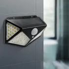 Luminária solar preta com painel, LEDs brancos e sensor de movimento na parede cinza.