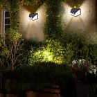 Duas luminárias solares pretas na parede iluminando jardim à noite.