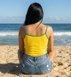 Regata Cropped Amarela com verde, mulher sentada na praia olhando o mar