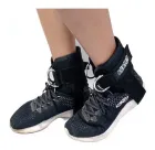 Tornozeleiras pretas com anéis metálicos em pernas calçando tênis escuros.